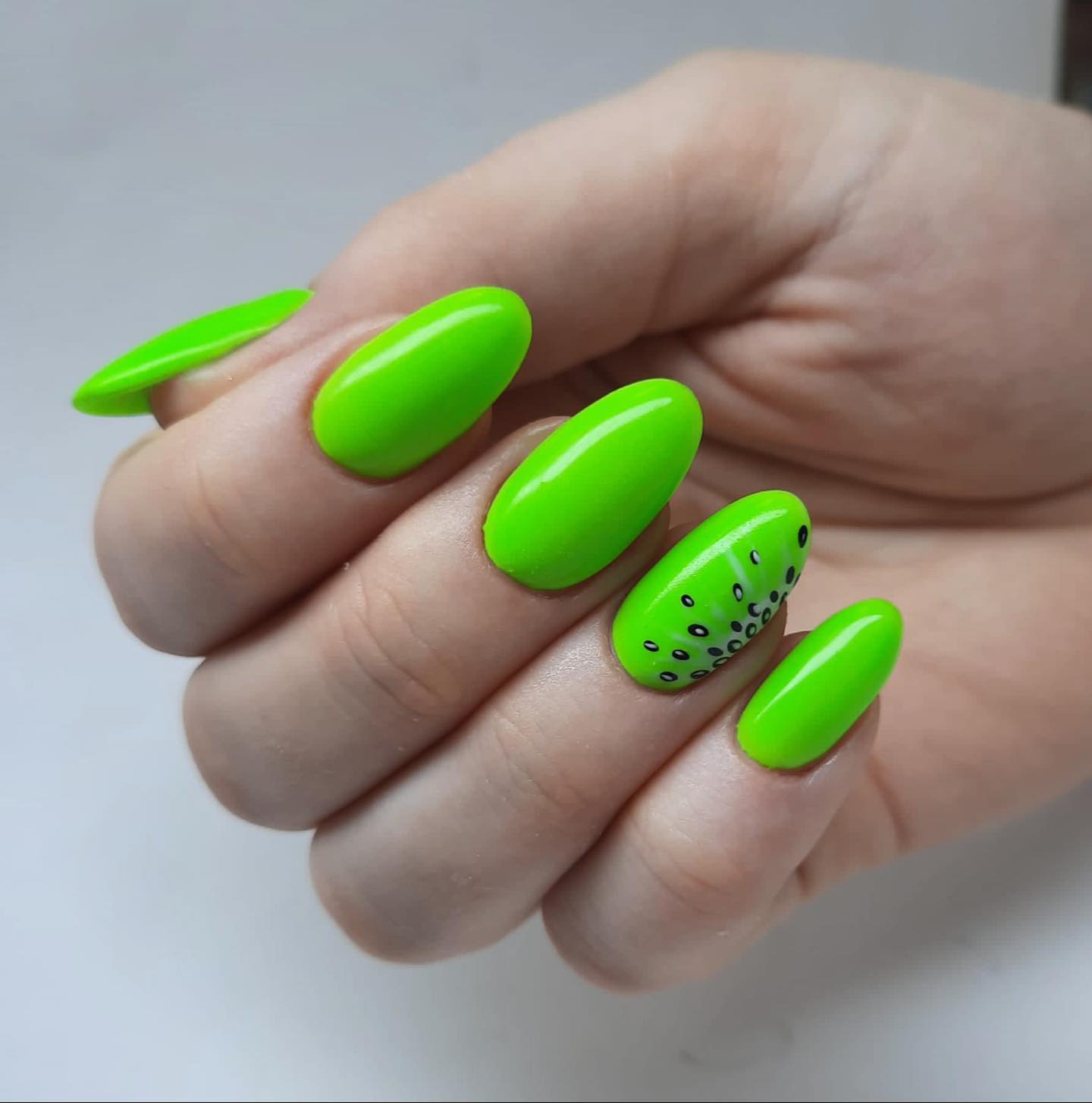 Zbliżenie limonkowo-zielonych owalnych paznokci z czarnymi wzorami na palcu serdecznym