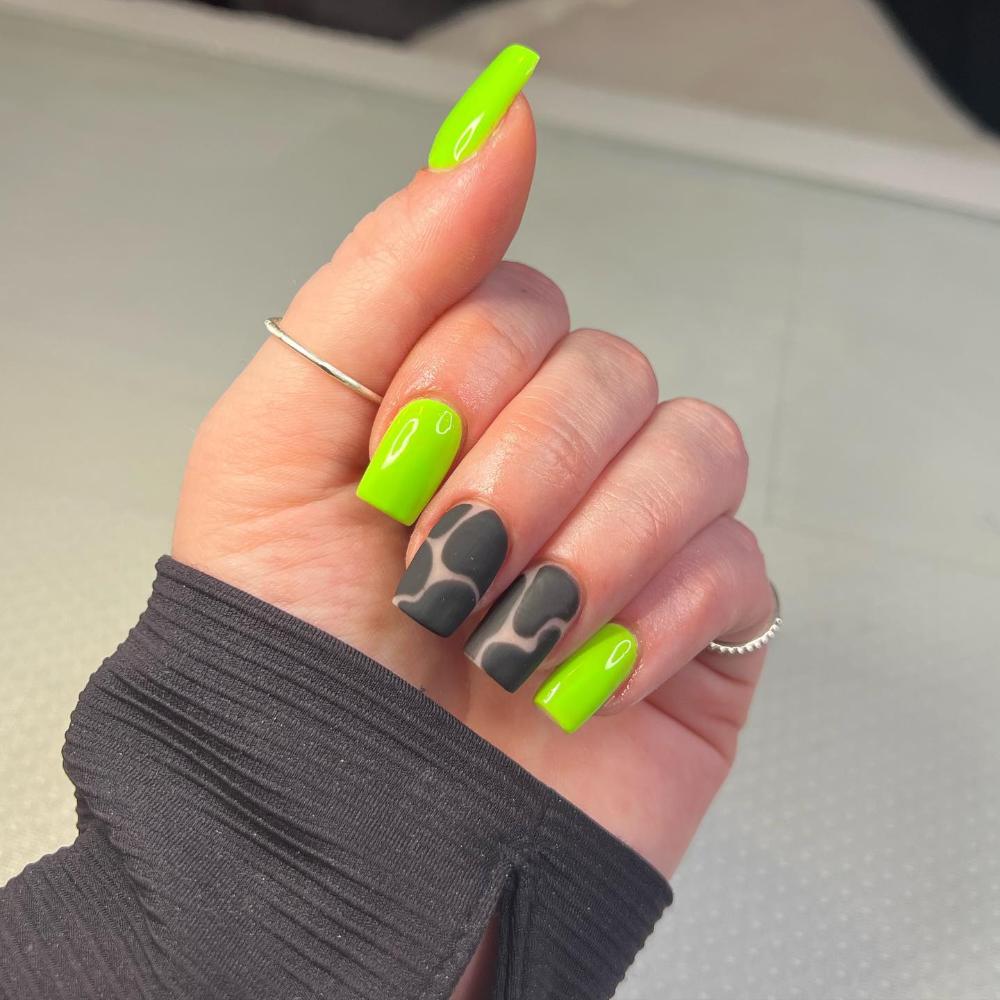 Zbliżenie neonowo zielonych paznokci w połączeniu z czarnymi matowymi wzorami