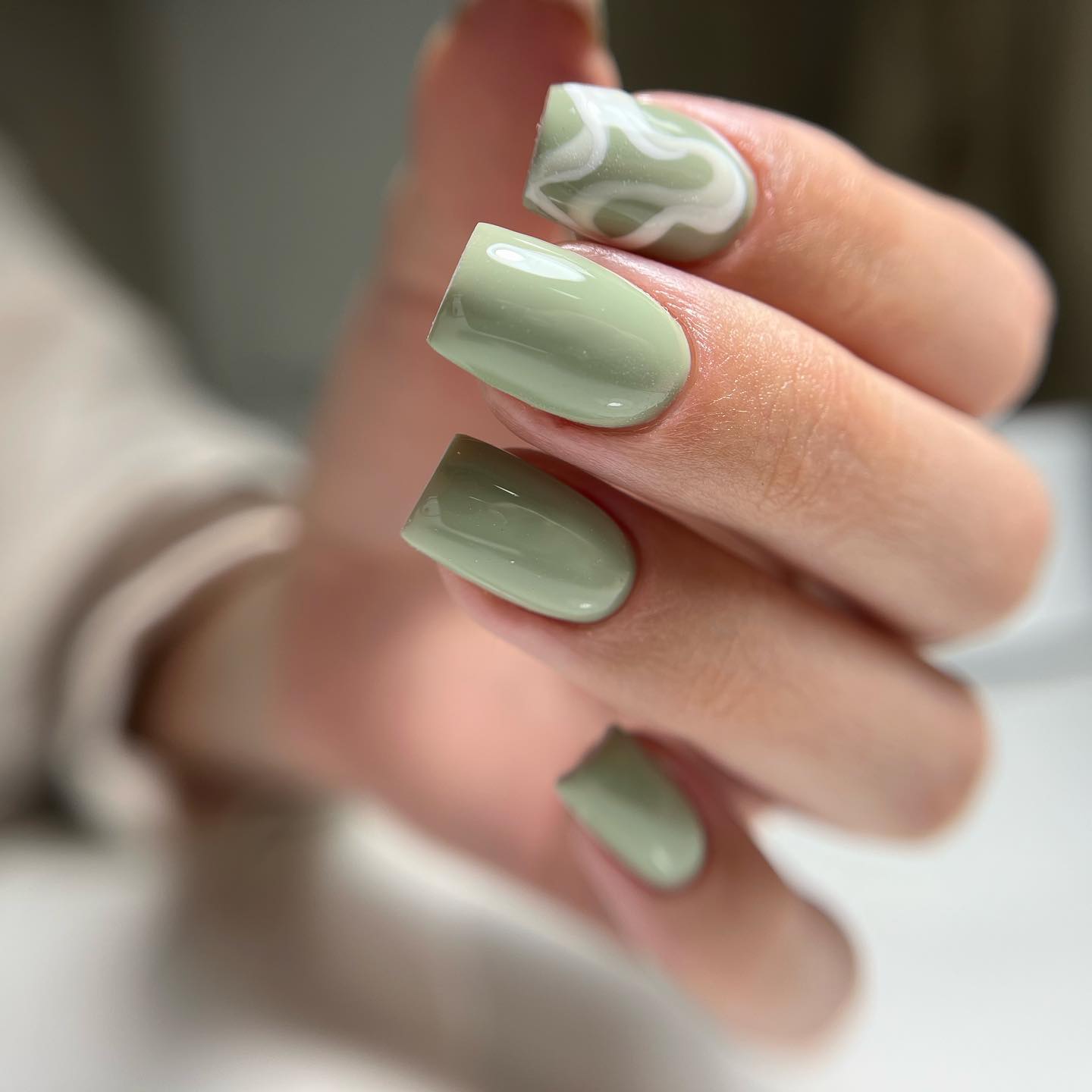 Eine Nahaufnahme hellgrüner quadratischer Nägel mit weißen abstrakten Gemälden auf dem Hauptfinger