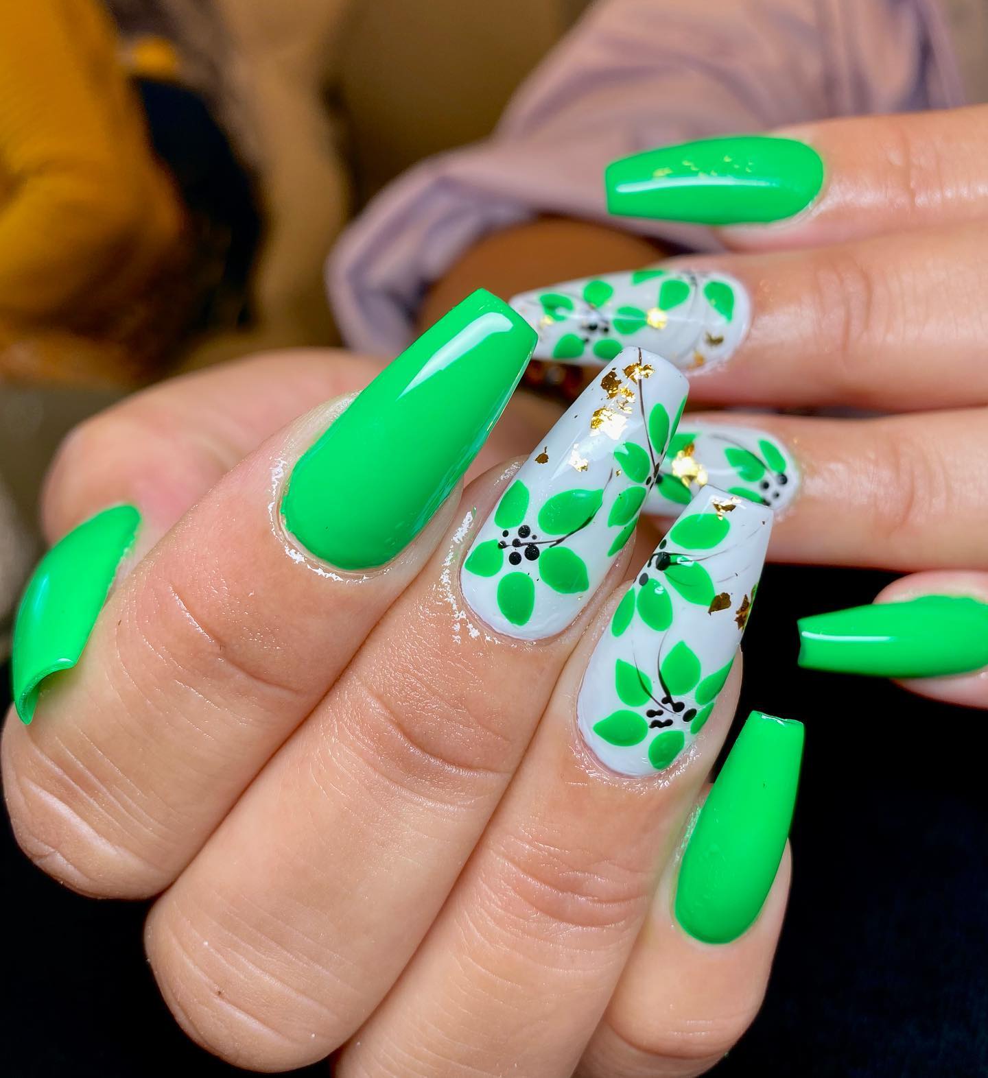 Eine Nahaufnahme hellgrüner und weißer Nägel mit floristischen Gemälden