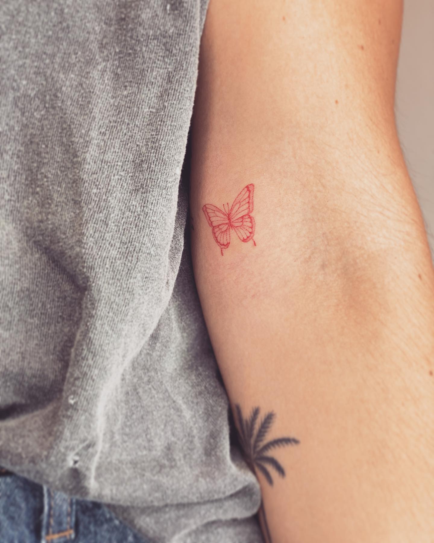 Cienki tatuaż z czerwonym motylem na ramieniu
