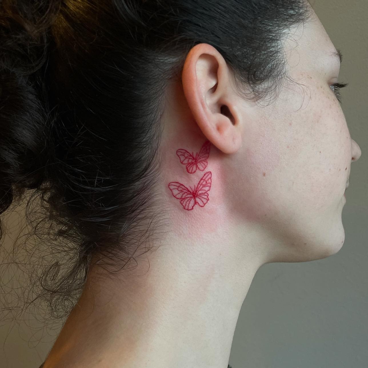 Czerwony tatuaż motyli za uchem