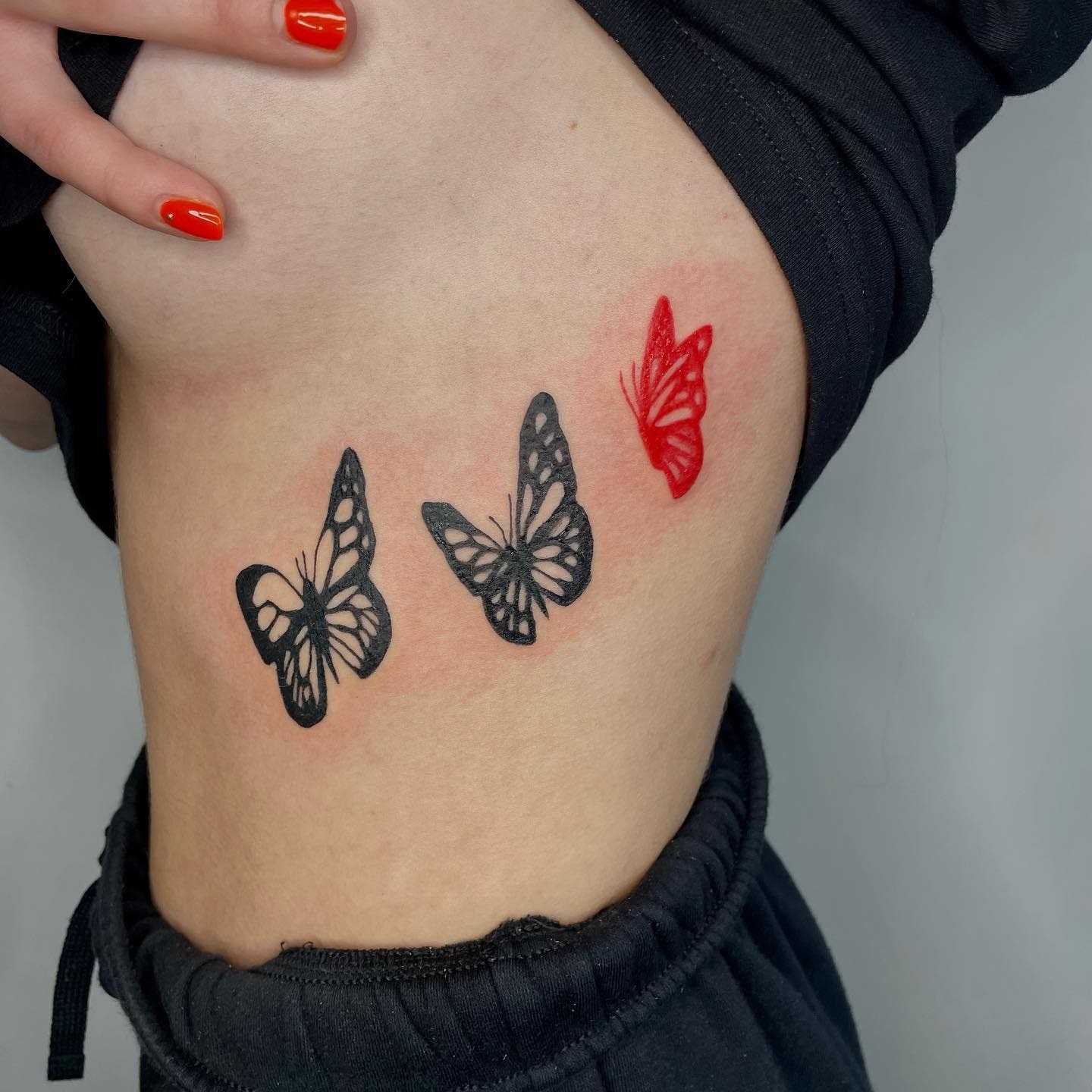 Tatuaż czerwono-czarnych motyli na żebrach