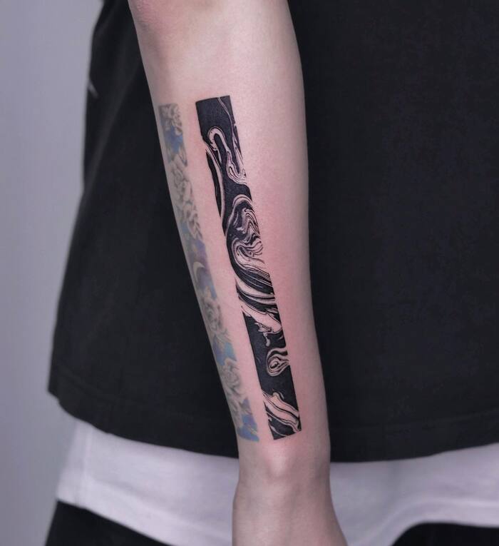Small blackout tattoo in form of abstract stripe on forearm