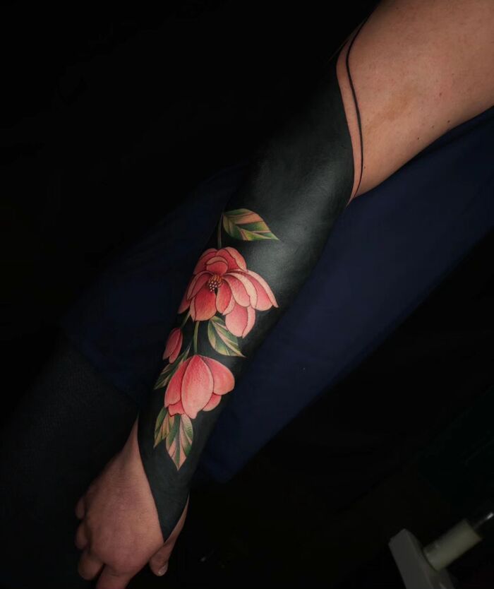 Blackout floral tattoo with red and green inks