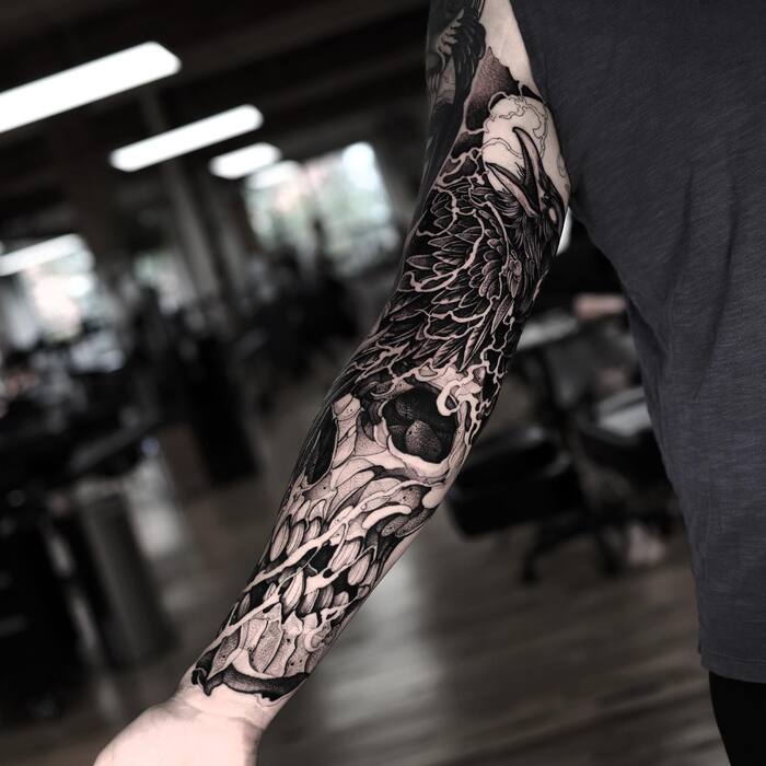 Blackout skull and raven tattoo on arm