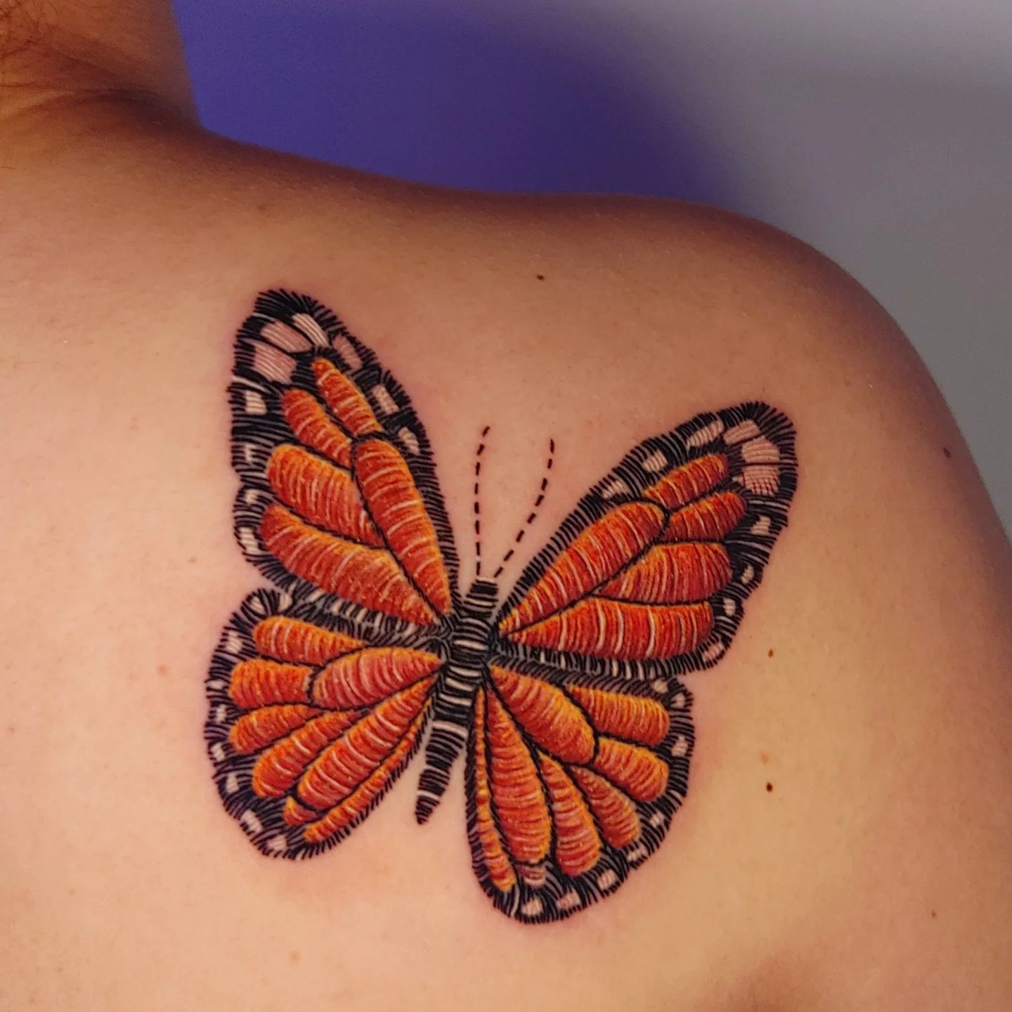 Orange butterfly stitch tattoo on shoulder