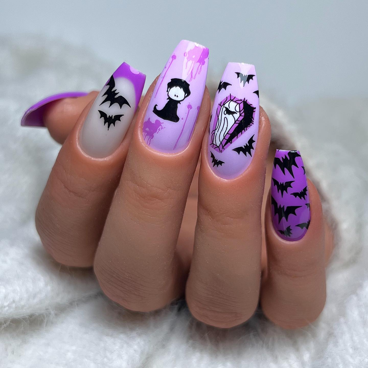 Kolejny przykład paznokci z motywem Halloween w kolorach fioletowym i czarnym z magicznymi kwiatami, księżycami, duchami, trumnami i czaszkami