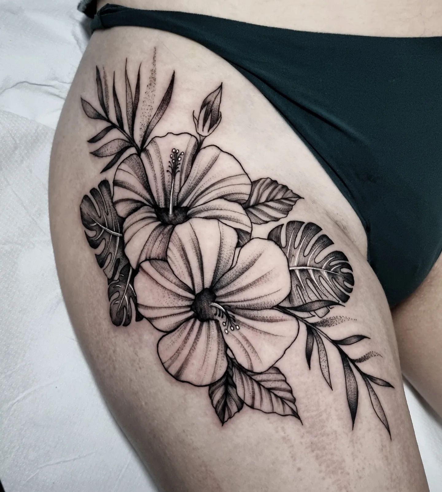 Черно-серая татуировка цветов в гавайском стиле на бедре