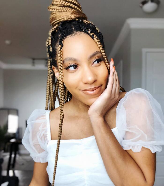 Honey blonde box braids with black roots and bun hairstyle