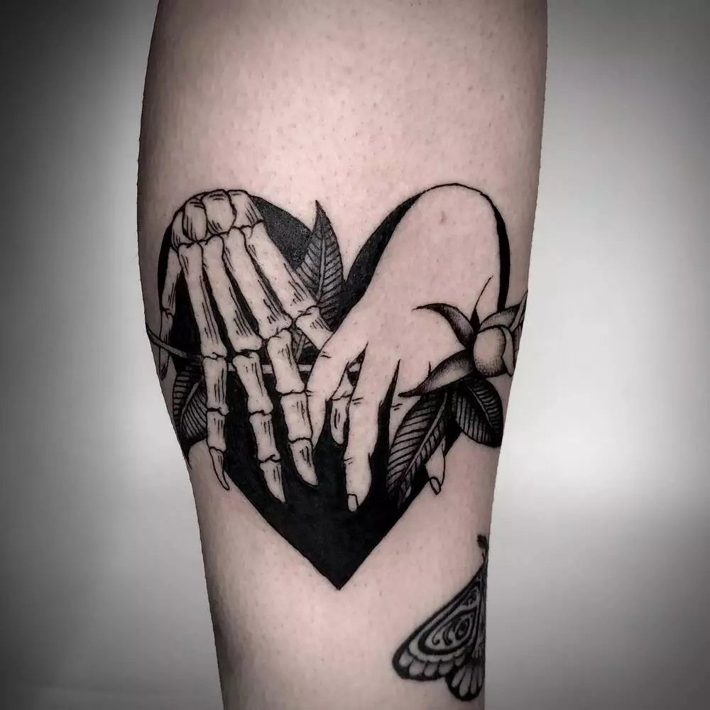 A Close-up Image of Skeleton Hand Holding Human Hand Tattoo With Black Heart Background