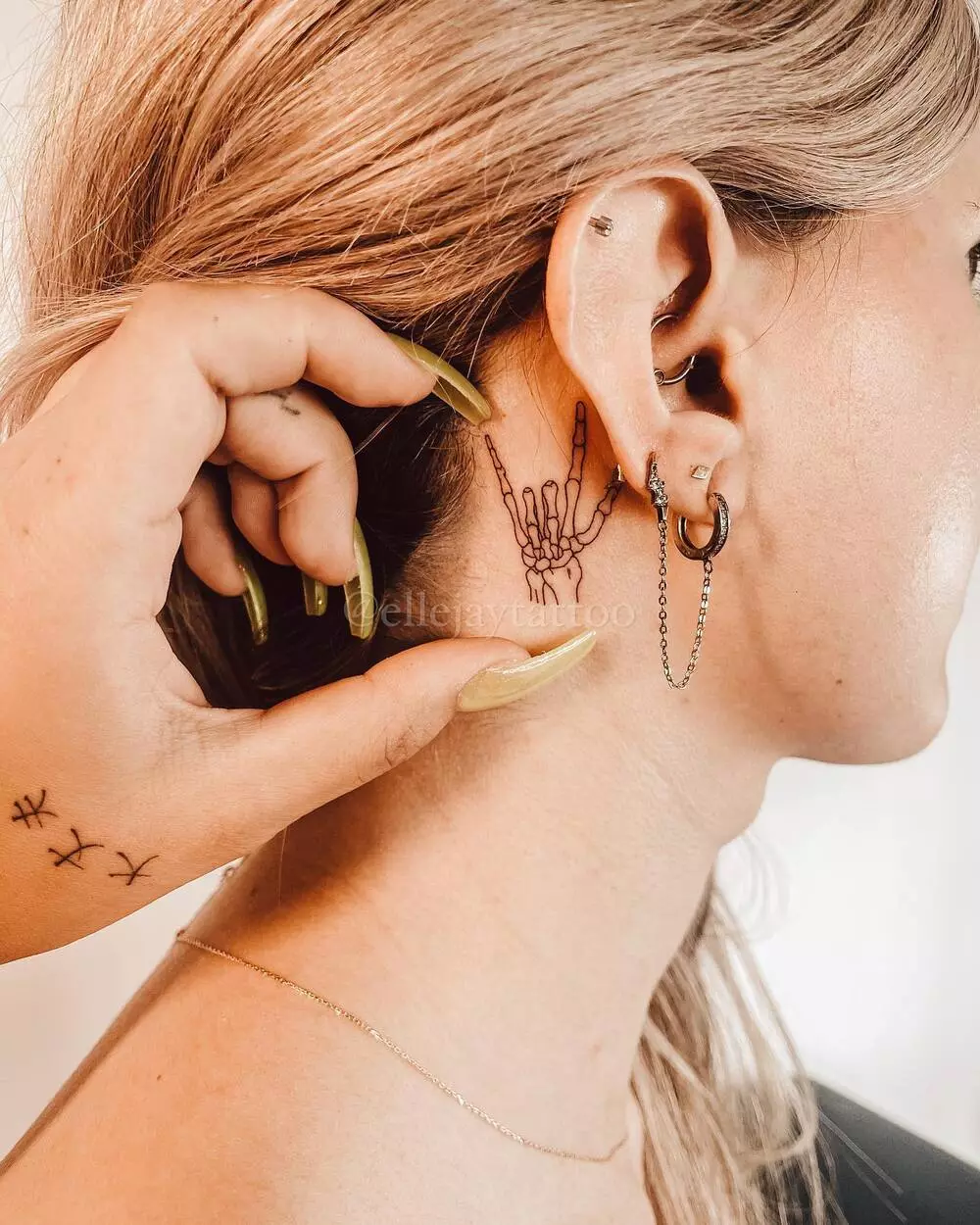 A Close-up Image of Small Skeleton Rock On Hand Tattoo Behind The Ear