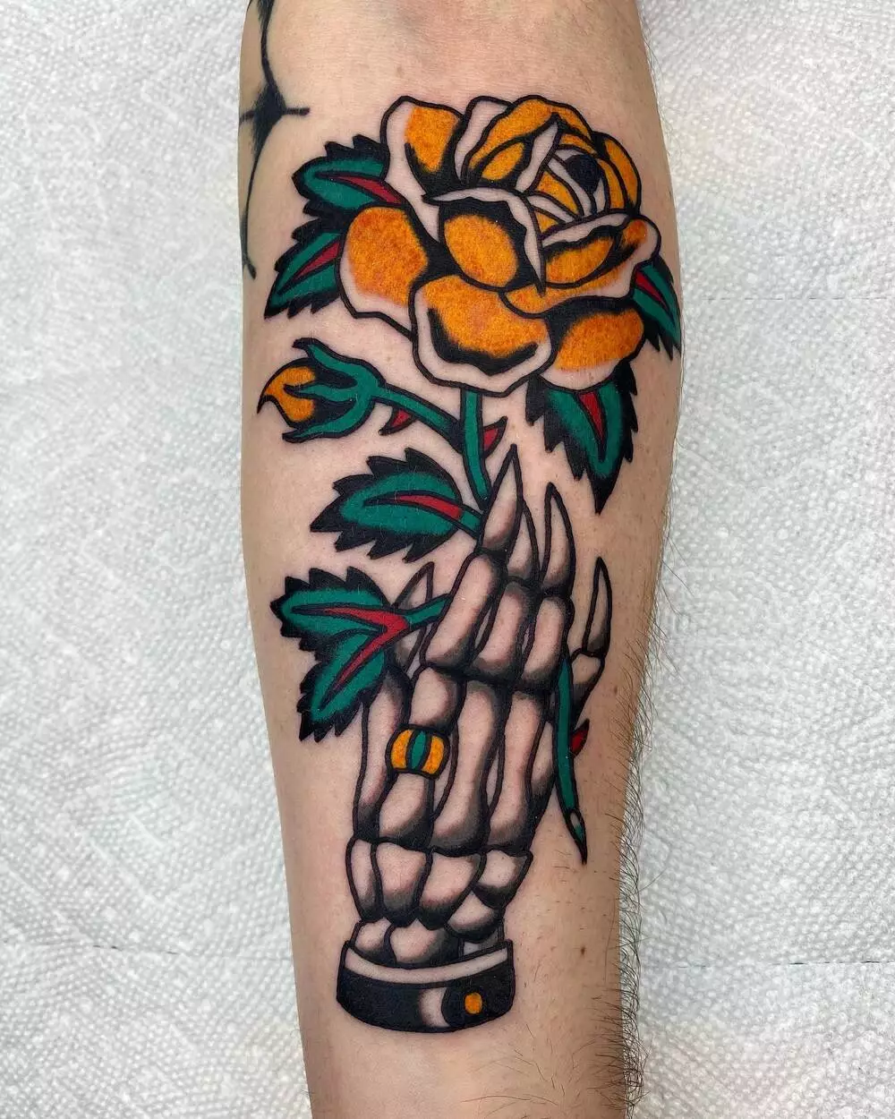 A Close-up Image of Traditional Skeleton Hand Holding Yellow Rose Tattoo