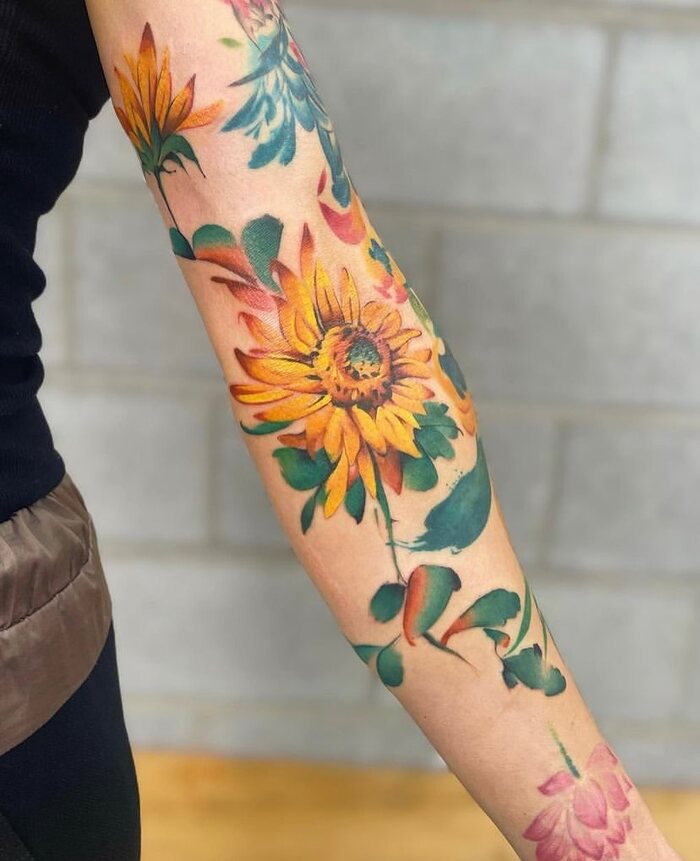 Watercolor tattoo of sunflower with leaves in orange and green inks