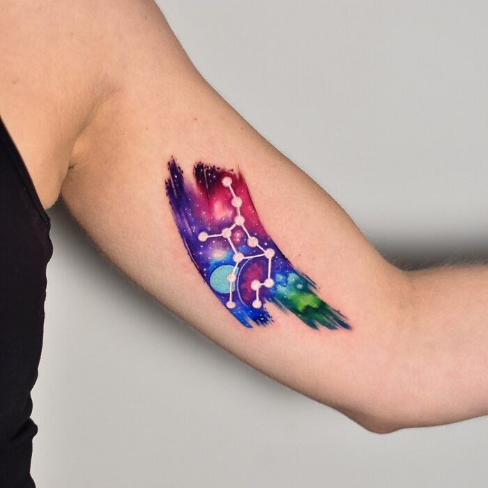 Tattoo of galaxy on multicolored background looking like watercolor stroke