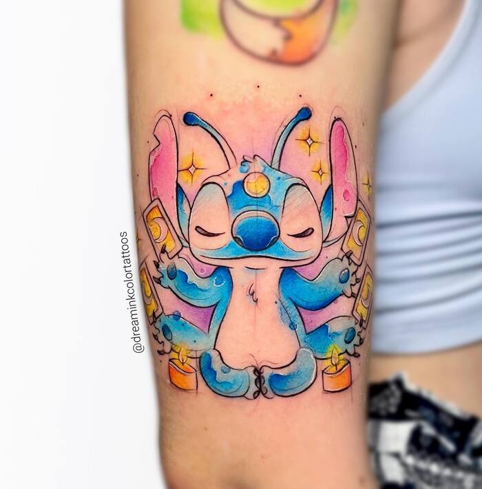 Watercolor tattoo of blue Stitch sitting in meditative pose and holding taro cards