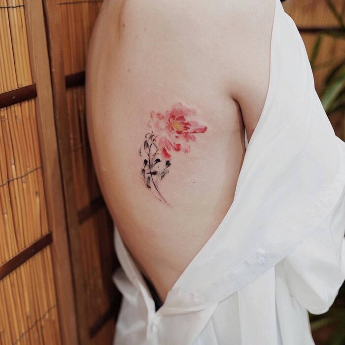 Watercolor tattoo of flower with red blossom and black stem on the back