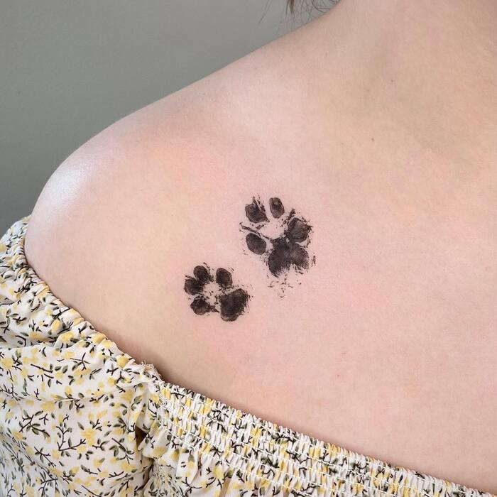 Watercolor tattoo of bigger and smaller dog and cat prints in black ink on collarbone
