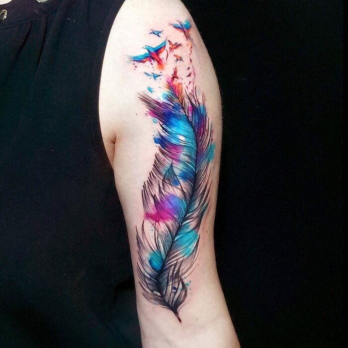 Tattoo of black feather with turquoise, blue and pink watercolor splashes on it