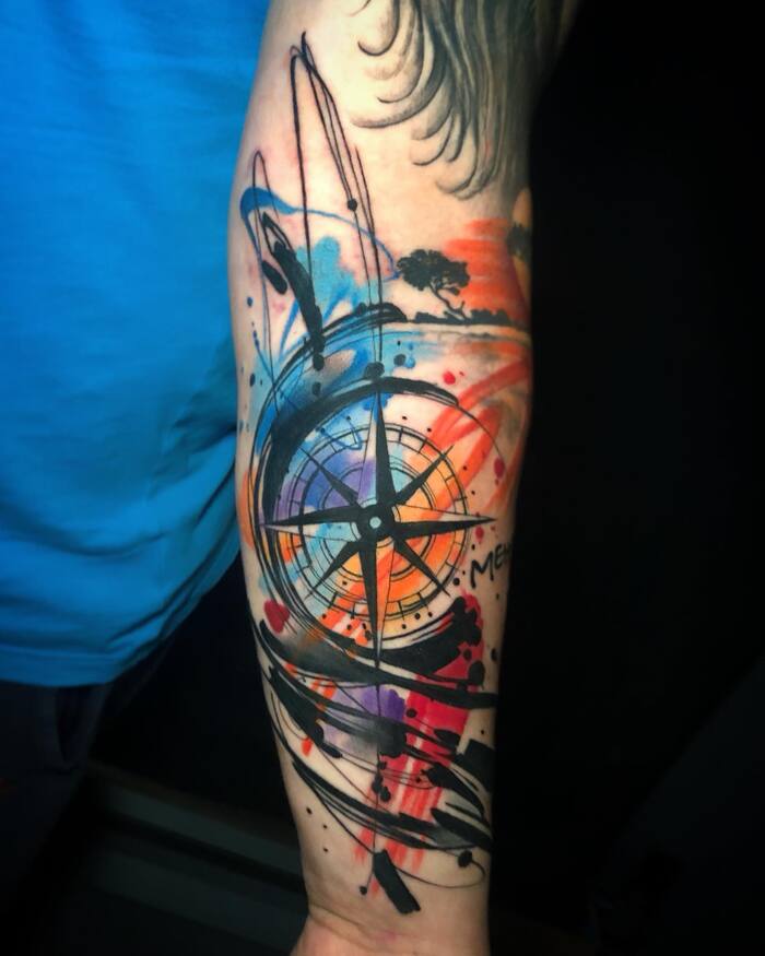 Tattoo of black compass surrounded by chaotic black and colored watercolor splashes