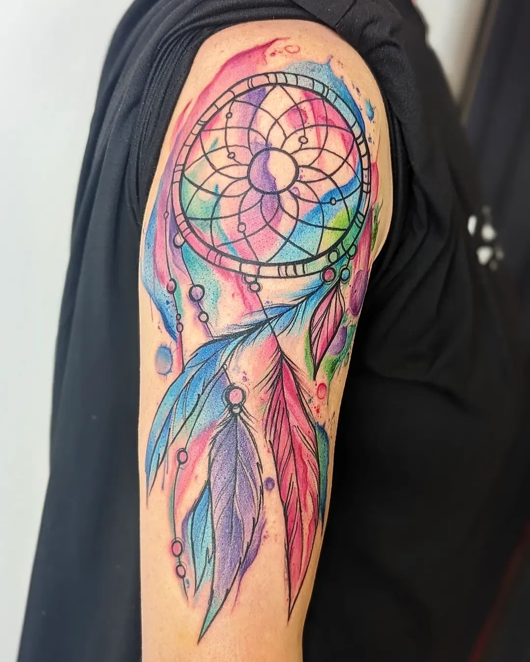 Akwarelowy tatuaż z dużym łapaczem snów na ramieniu w różnych kolorach