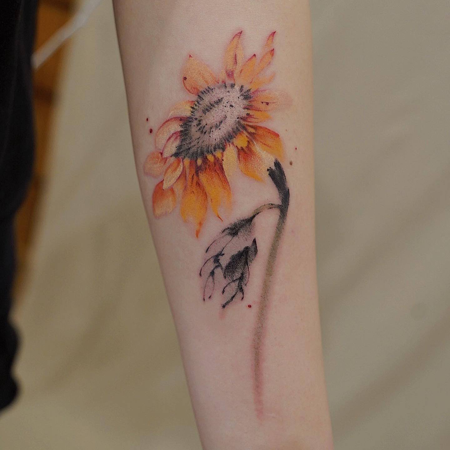 Akwarelowy tatuaż przedstawiający słonecznik z wyblakłymi pomarańczowymi płatkami i czarną rufą