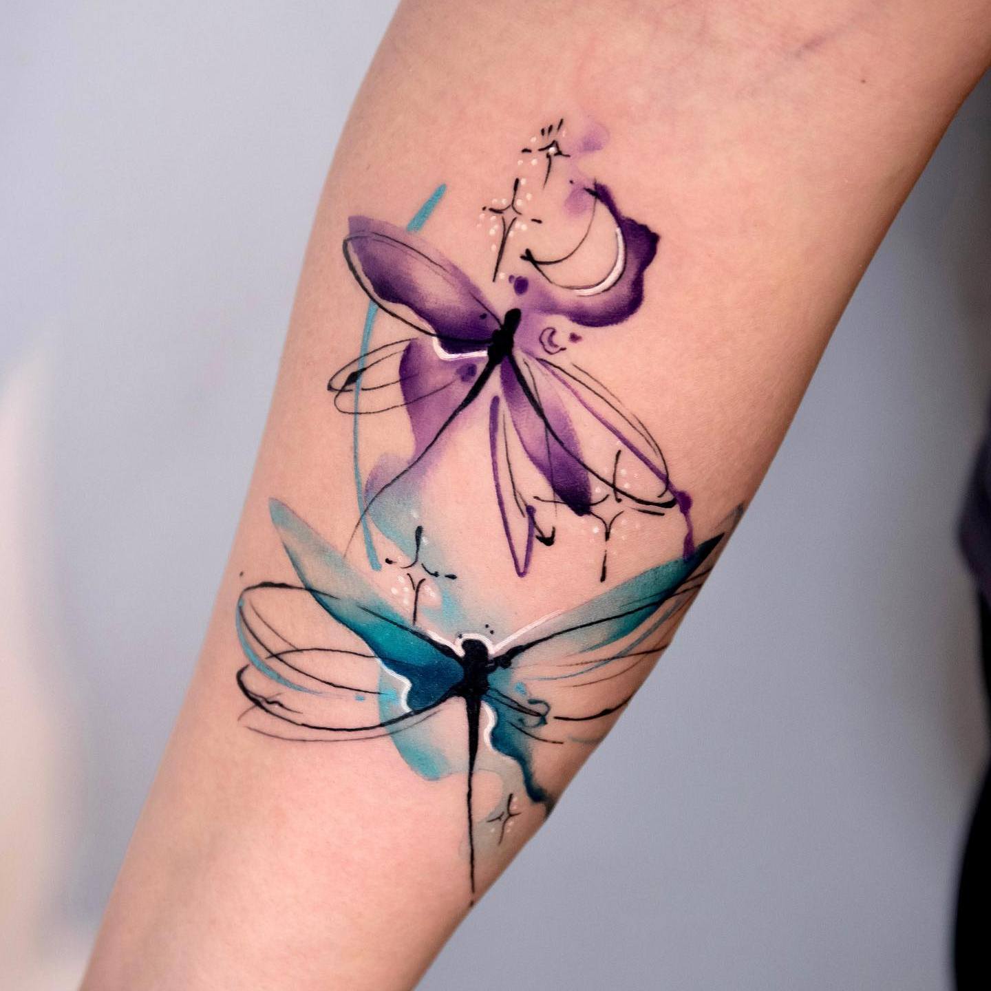 Akwarelowy tatuaż przedstawiający dwie ważki w spokojnych kolorach niebieskim i fioletowym