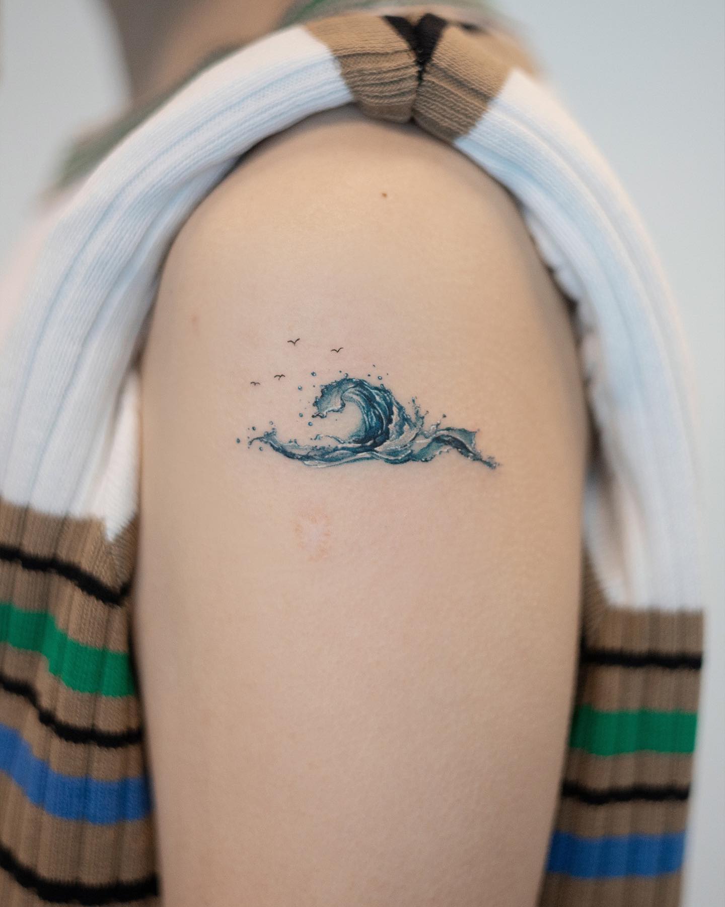 Akwarelowy tatuaż przedstawiający minimalistyczną falę oceaniczną w ciemnoniebieskich i białych kolorach
