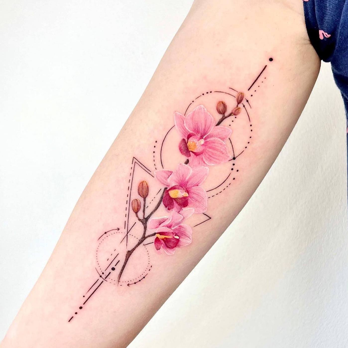 Akwarelowy tatuaż przedstawiający różowe kwiaty orchidei na brązowej łodydze otoczonej geometrycznymi kształtami