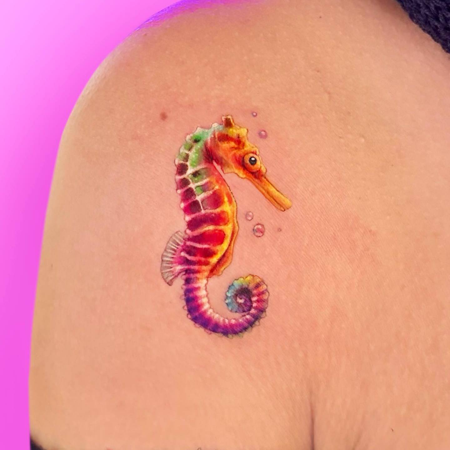 Akwarelowy tatuaż przedstawiający małego konika morskiego w jasnych kolorach na ramieniu