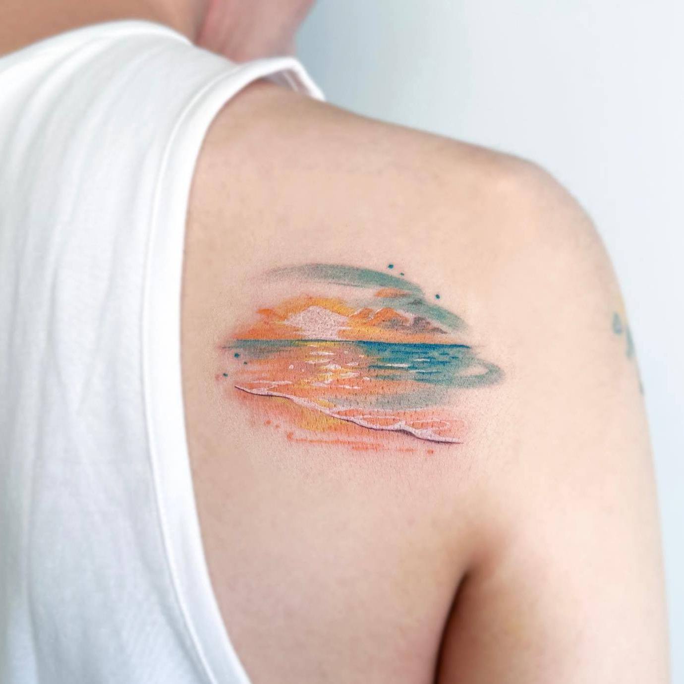 Akwarelowy tatuaż przedstawiający zachód słońca w spokojnych odcieniach pomarańczu i błękitu