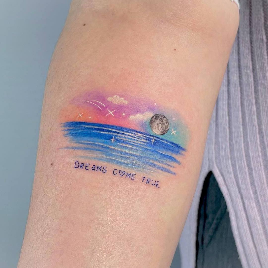Akwarela tatuaż przedstawiający ocean z cytatem „Spełnienie marzeń”.