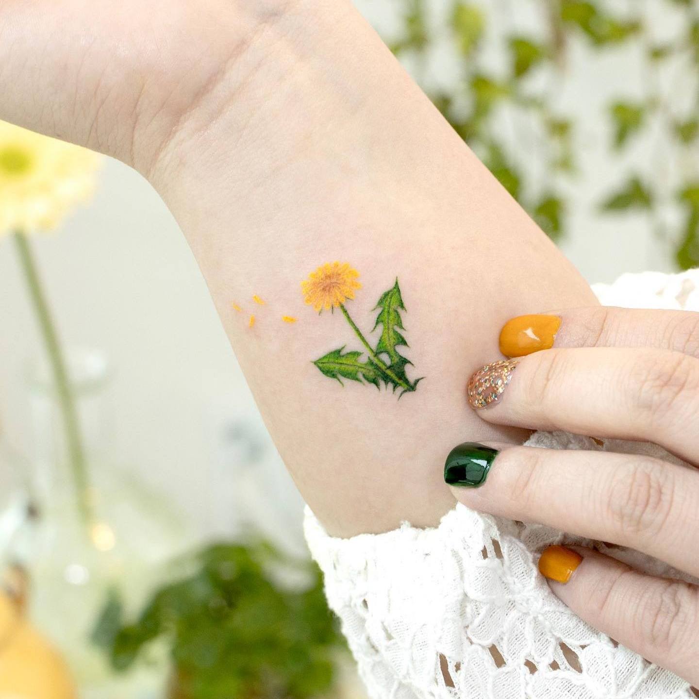 Akwarelowy tatuaż przedstawiający żółty kwiat mniszka lekarskiego z zieloną łodygą i liśćmi
