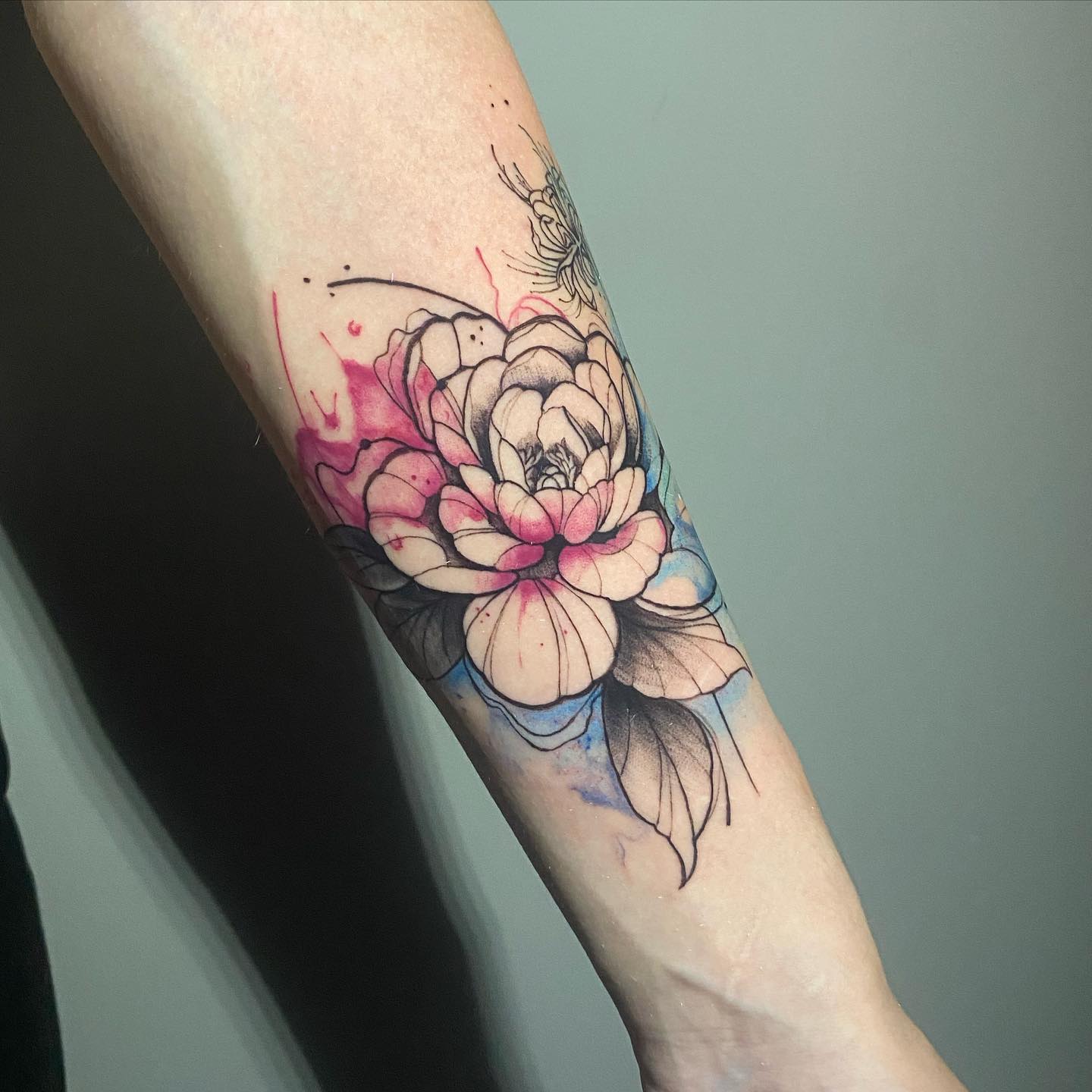 Akwarelowy tatuaż przedstawiający kwiat czarnej piwonii z ciemnoróżowymi i niebieskimi plamami